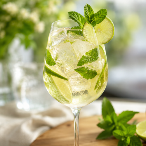 Hugo Spritz cocktail with prosecco, elderflower, fresh mint, lime slices and ice in a wine glass.